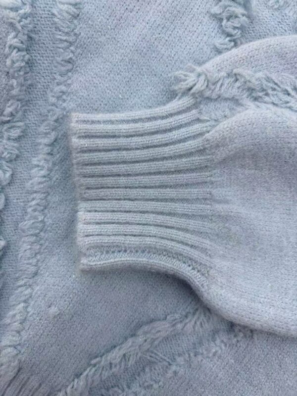 Close-up of a light blue knit sweater showing detailed stitching and ribbed cuff, highlighting cozy fabric and craftsmanship.