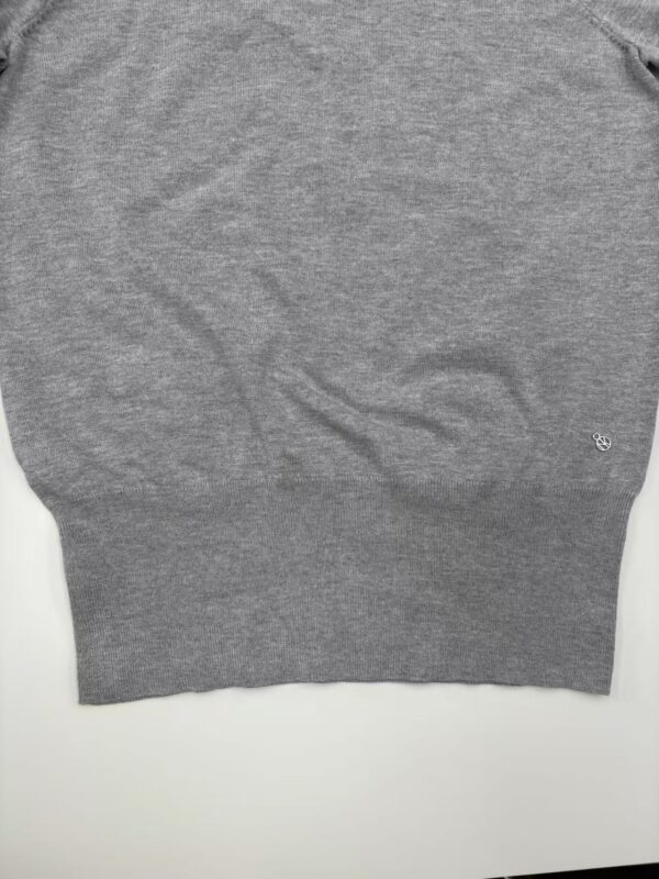 Close-up of a gray knitted sweater with a small embroidered logo on the lower right side, suitable for casual fashion.