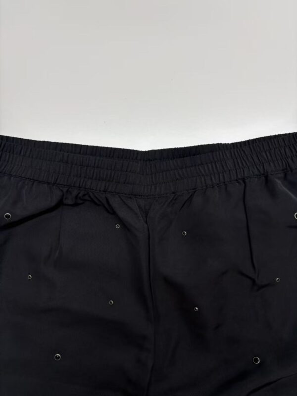 Close-up of black shorts featuring eyelet embellishments and elastic waistband, perfect for casual or athletic wear.