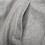 Close-up of a gray wool coat pocket with a sleek, minimalist design, showcasing fine stitching and fabric texture.