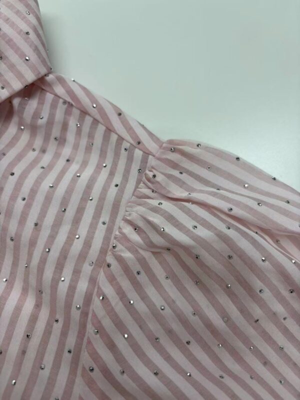 Close-up of a pink and white striped dress with silver embellishments, showcasing fabric details and design elements.