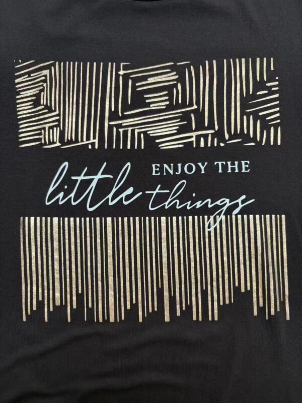 Black T-shirt featuring a modern geometric design with the phrase "Enjoy the little things" in stylish fonts.