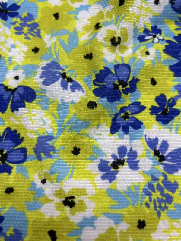 Colorful floral fabric with blue, white, and yellow flowers and green leaves, suitable for fashion and home decor.