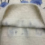 Close-up of a cream-colored knit sweater with a folded collar, showing detailed ribbing and soft fabric texture.