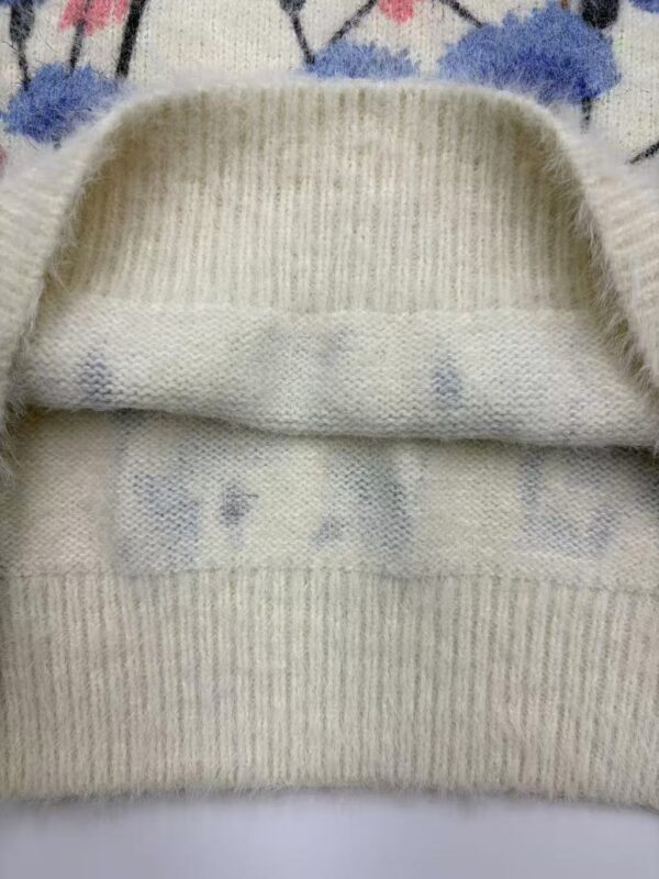 Close-up of a cream-colored knit sweater with a folded collar, showing detailed ribbing and soft fabric texture.
