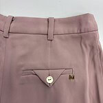 Close-up of pink women's dress pants featuring a buttoned back pocket with a small gold 'M' logo, suitable for formal or office wear.