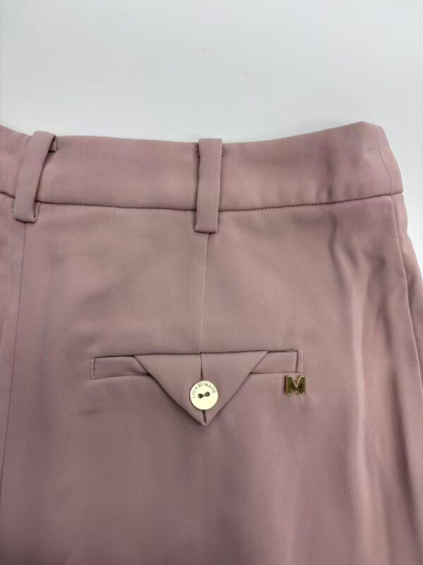 Close-up of pink women's dress pants featuring a buttoned back pocket with a small gold 'M' logo, suitable for formal or office wear.