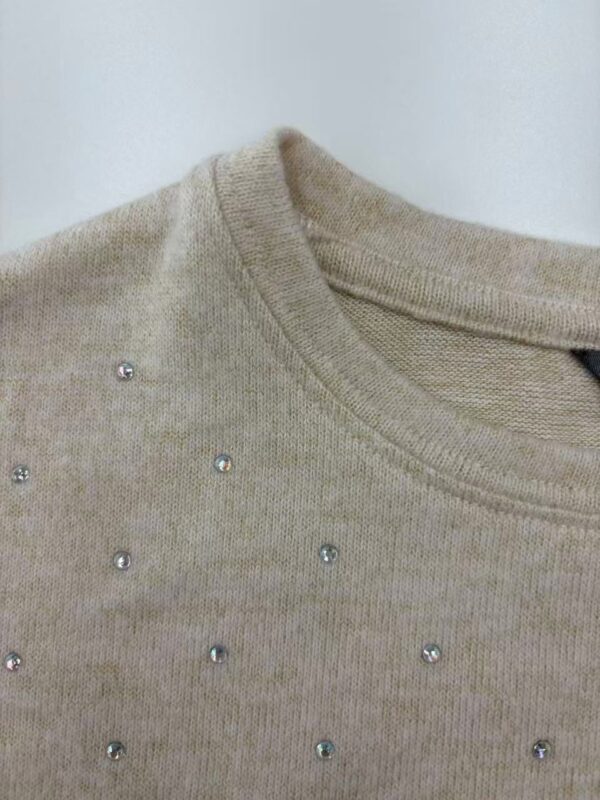 Close-up of a beige sweater adorned with small rhinestones around the neckline, showcasing elegant casual fashion for women.