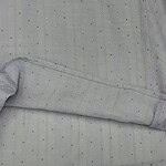 Close-up of light grey fabric with small, shiny embellishments, showcasing fine texture and detailed craftsmanship for fashion or textile design.
