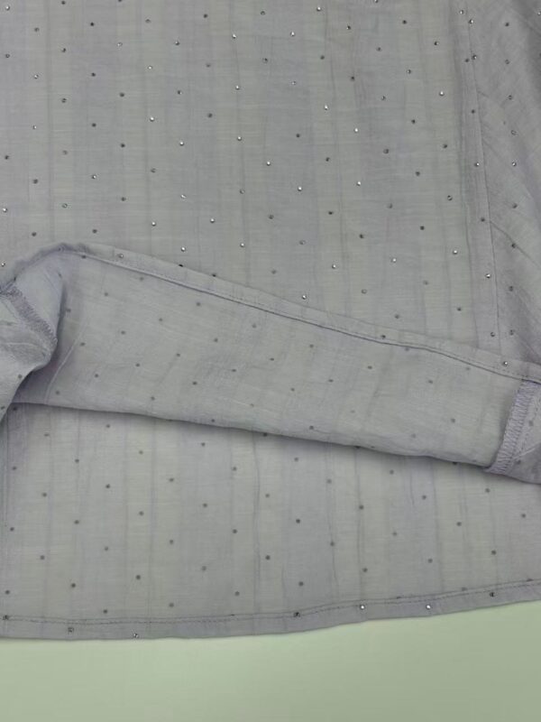 Close-up of light grey fabric with small, shiny embellishments, showcasing fine texture and detailed craftsmanship for fashion or textile design.