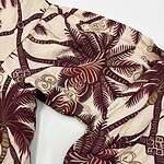 Close-up of tropical-themed fabric with palm leaves and geometric patterns in beige and maroon colors, suitable for clothing or accessories.
