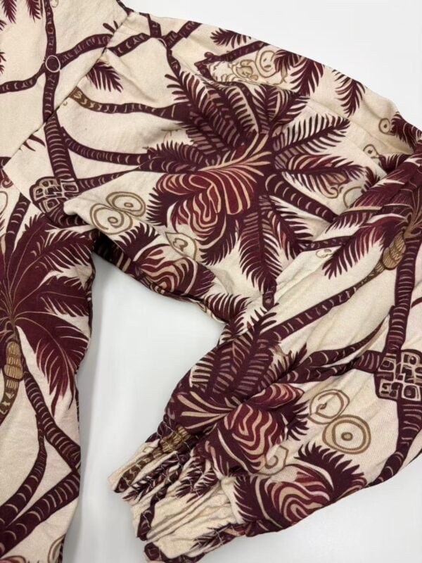 Close-up of tropical-themed fabric with palm leaves and geometric patterns in beige and maroon colors, suitable for clothing or accessories.