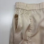 Close-up of beige satin lounge pants with elastic waistband, showcasing smooth fabric and comfortable fit, ideal for casual or loungewear.