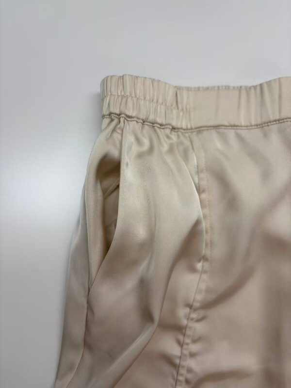 Close-up of beige satin lounge pants with elastic waistband, showcasing smooth fabric and comfortable fit, ideal for casual or loungewear.