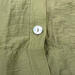 Close-up of an olive green linen shirt showing detailed stitching and a single iridescent button.