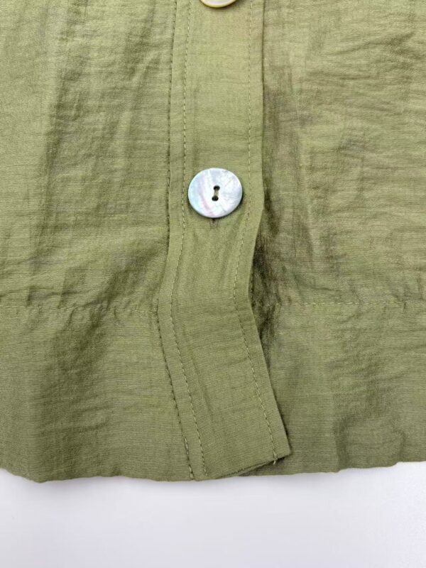 Close-up of an olive green linen shirt showing detailed stitching and a single iridescent button.