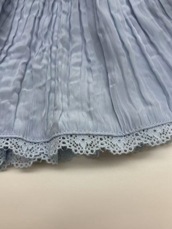 Close-up of a light blue pleated skirt featuring delicate lace trim at the hem, showcasing elegant fabric details and craftsmanship.