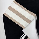 Close-up of a black sweater with beige and white horizontal stripes on the sleeve, featuring ribbed cuffs with black and white stripes, perfect for casual fashion.