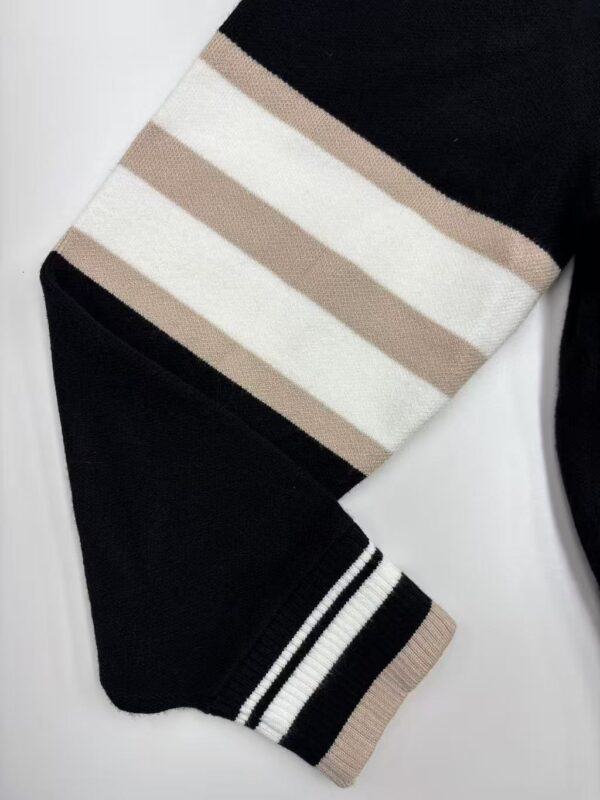 Close-up of a black sweater with beige and white horizontal stripes on the sleeve, featuring ribbed cuffs with black and white stripes, perfect for casual fashion.