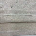 Close-up of beige fabric with small, shiny beads creating a subtle decorative pattern, showcasing fine textile craftsmanship.