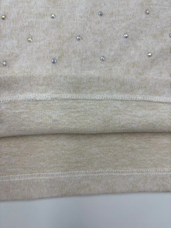 Close-up of beige fabric with small, shiny beads creating a subtle decorative pattern, showcasing fine textile craftsmanship.