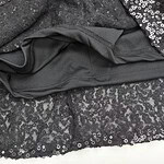 Close-up of a black sequin dress with a smooth black lining visible at the hem, showcasing shiny sequins and elegant fabric details.