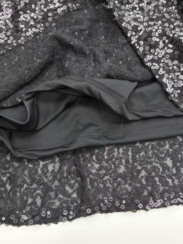 Close-up of a black sequin dress with a smooth black lining visible at the hem, showcasing shiny sequins and elegant fabric details.