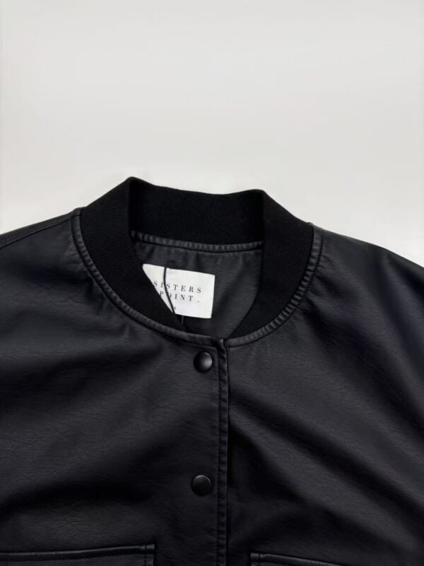 Close-up of a black leather bomber jacket with snap buttons and ribbed collar, perfect for fashion-forward casual wear.