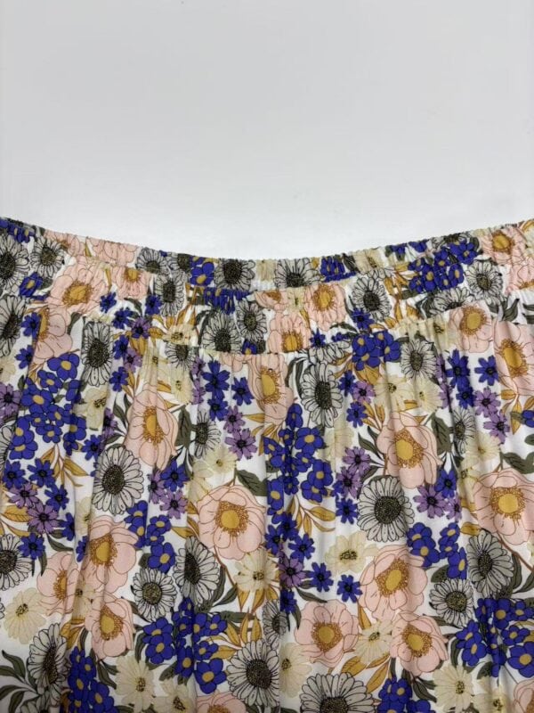 Close-up of a floral patterned skirt with pink, blue, and black flowers on a light background, featuring an elastic waistband.