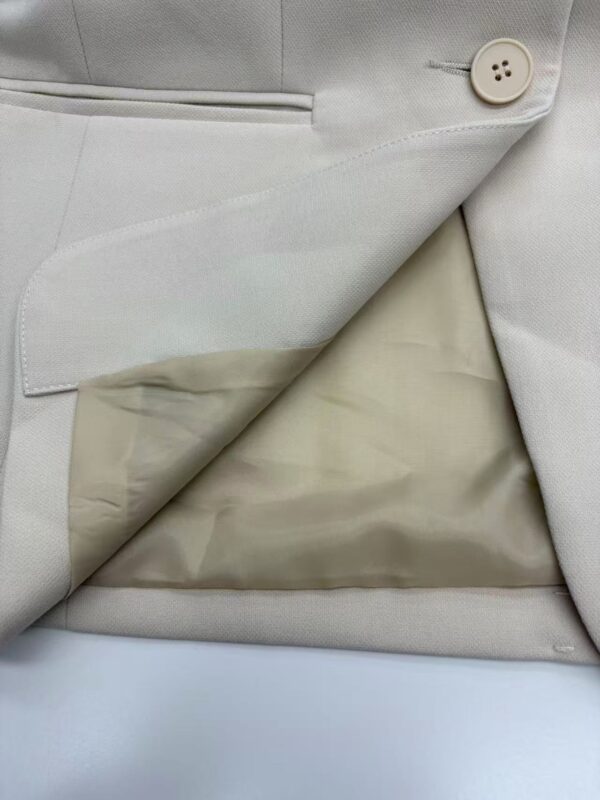 Close-up of a light beige suit jacket with a single button and inner lining visible, showcasing high-quality tailoring and fabric.