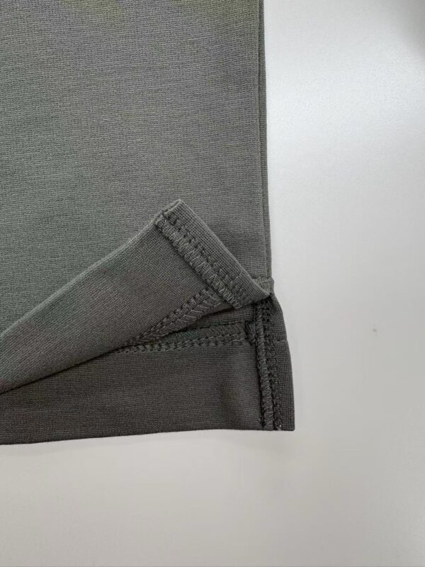 Detailed view of the stitched edge of a grey fabric material, showing clean stitching and smooth texture, suitable for clothing or upholstery.
