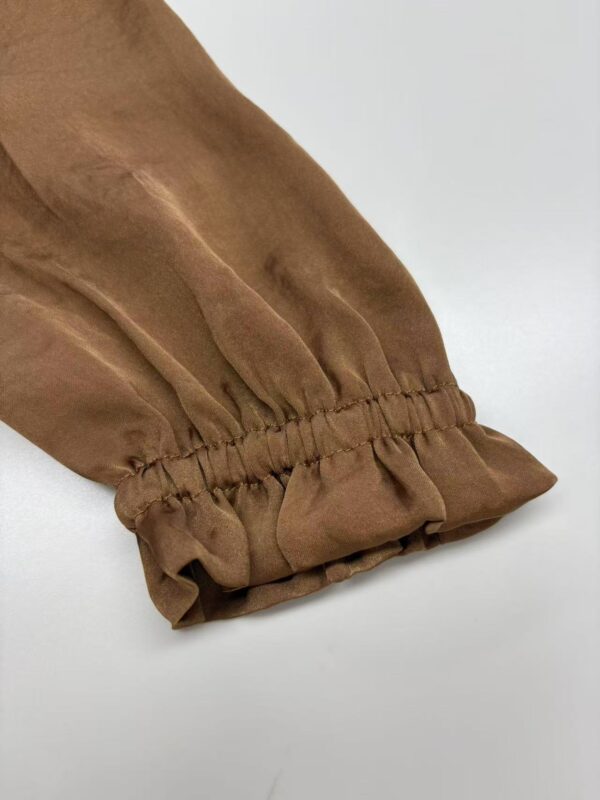 Close-up of a brown fabric sleeve with gathered elastic cuff, showcasing stylish and comfortable design suitable for fashion-forward outfits.