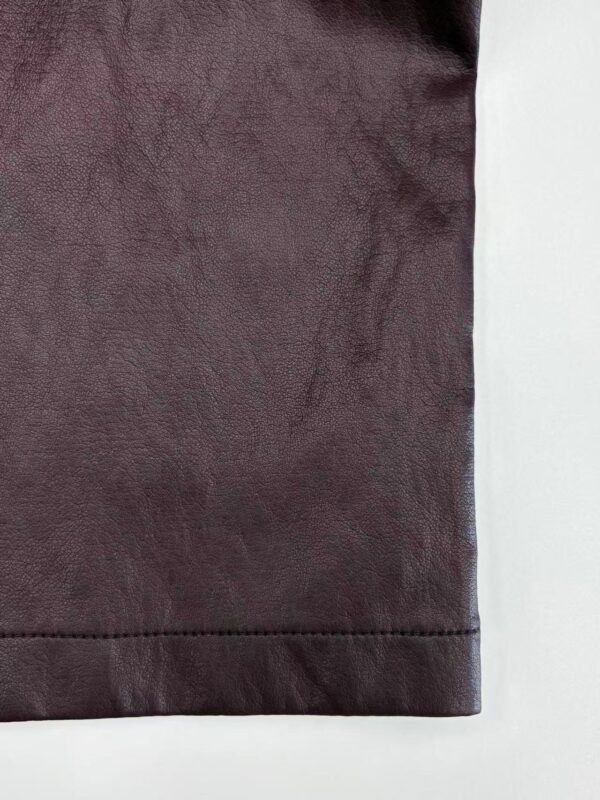 Detailed view of burgundy leather fabric with visible texture and stitching, ideal for fashion and accessory design.