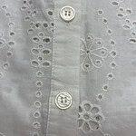 Close-up of a white shirt with intricate eyelet embroidery and two white buttons, showcasing detailed craftsmanship and delicate fabric.