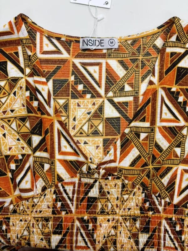 Close-up of a dress with a vibrant geometric pattern in orange, black, white, and yellow colors, featuring intricate triangles and lines.