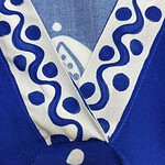Close-up of a blue fabric with white decorative patterns, featuring a folded edge and a circular button detail, showcasing intricate design and craftsmanship.