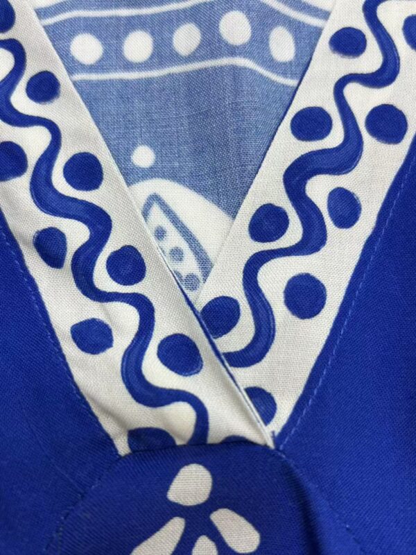 Close-up of a blue fabric with white decorative patterns, featuring a folded edge and a circular button detail, showcasing intricate design and craftsmanship.