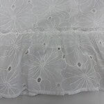 Close-up of white fabric with intricate embroidered floral patterns and small cut-out details, ideal for fashion or home decor projects.