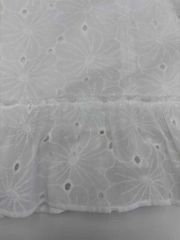 Close-up of white fabric with intricate embroidered floral patterns and small cut-out details, ideal for fashion or home decor projects.