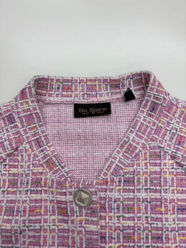 Close-up of a pink tweed women's jacket with a silver button, featuring a textured pattern and a black label inside reading 'So Soire' for fashion and style.