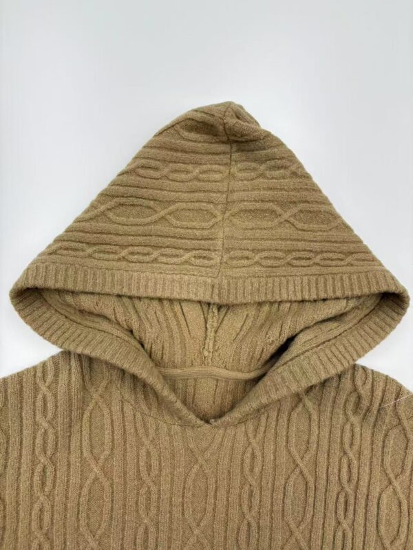 Close-up of a beige cable knit hoodie with a hood, showcasing detailed knitting patterns and texture, perfect for casual winter wear.