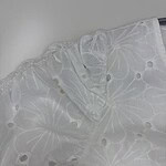 Close-up of white embroidered fabric with floral patterns and eyelet details, perfect for fashion and dressmaking.
