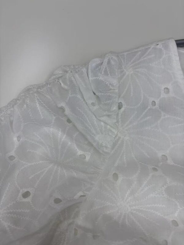 Close-up of white embroidered fabric with floral patterns and eyelet details, perfect for fashion and dressmaking.