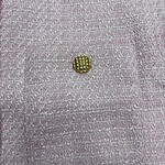 Close-up of pink textured fabric featuring a small gold button, highlighting luxury fashion details and craftsmanship.