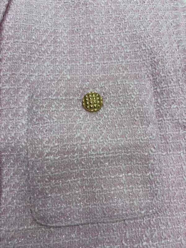 Close-up of pink textured fabric featuring a small gold button, highlighting luxury fashion details and craftsmanship.