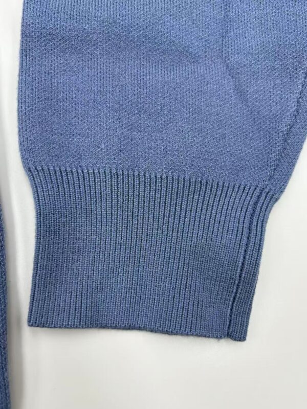 Close-up of a blue knitted sweater sleeve showing fine texture and ribbed cuff, ideal for casual or stylish winter wear.