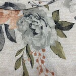 Close-up of fabric with floral print featuring a large white flower, green leaves, and orange accents, suitable for clothing or home decor.