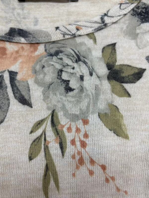 Close-up of fabric with floral print featuring a large white flower, green leaves, and orange accents, suitable for clothing or home decor.