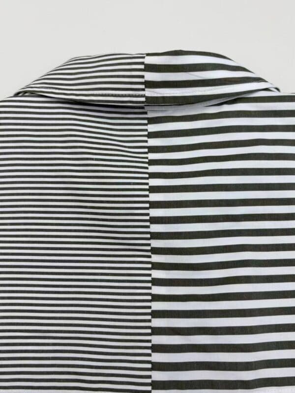 Close-up of a black and white striped shirt with a collar, showcasing contrasting stripe patterns on each side.