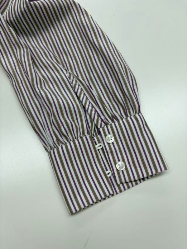 Close-up of a striped shirt cuff featuring vertical multicolor stripes and four white buttons, showcasing stylish and elegant design details.